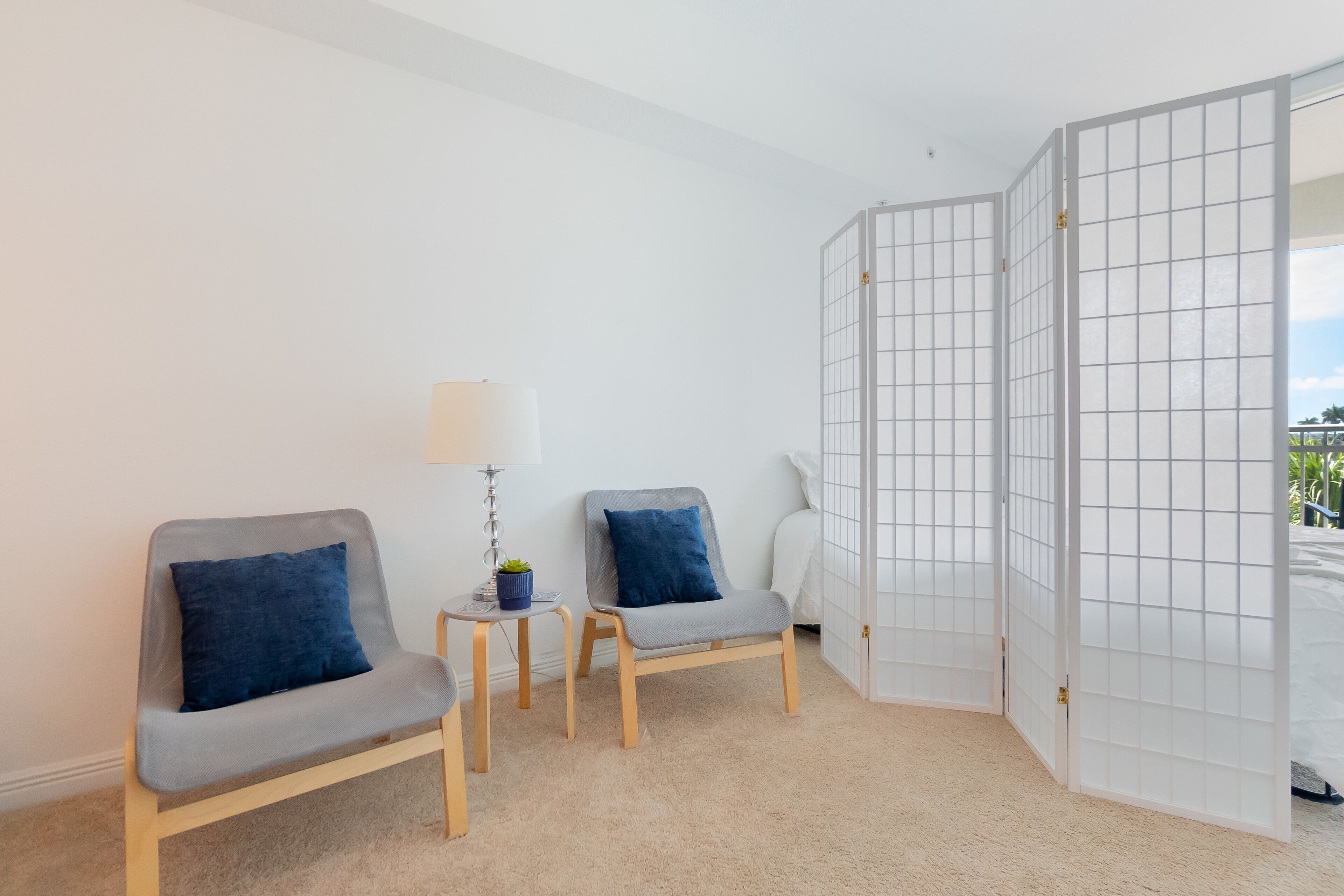 A room with two grey chairs, a small table with a lamp, and a white partition.