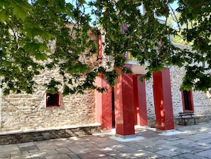 A stone building with red pillars and a bench. - Zina s Cottage in Afetes (South Pelion)