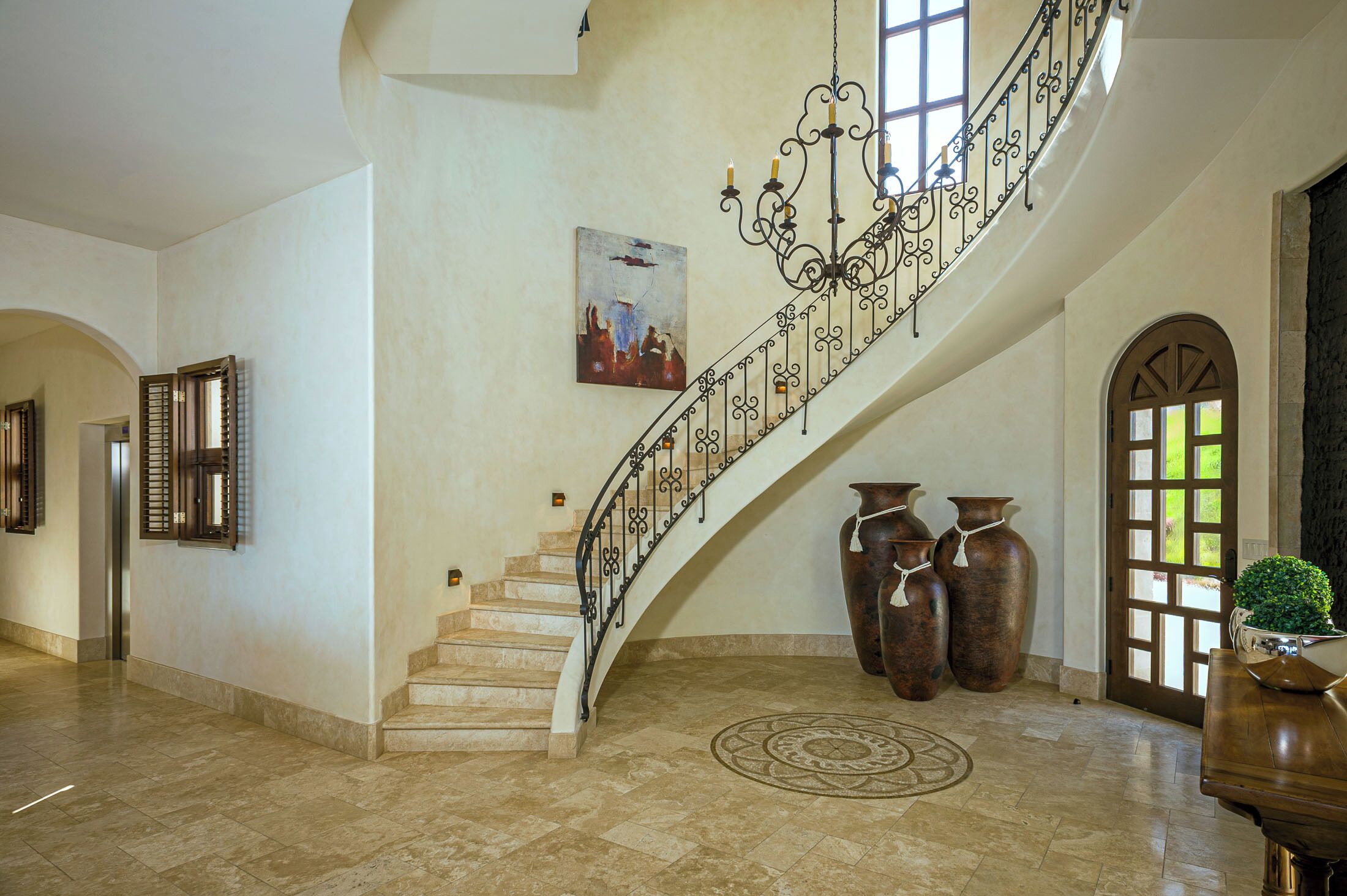 A grand staircase with a wrought iron railing, large vases, and a piano in a spacious lobby area.