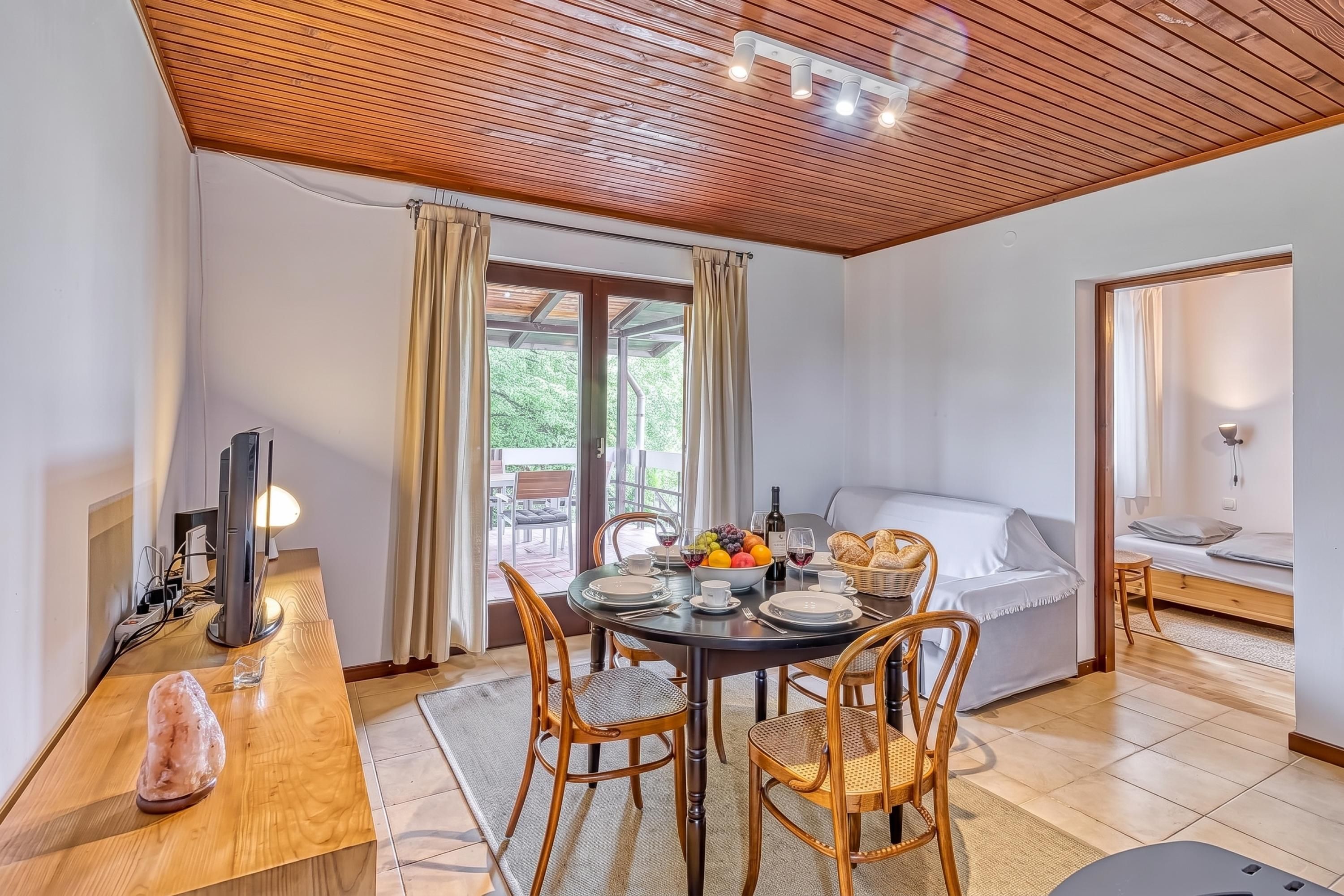 Una habitación acogedora con techo de madera, una mesa de comedor con sillas, una cama y un televisor.
