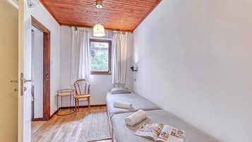 A small, cozy room with a wooden ceiling, a single bed, a chair, a small table, and a window with curtains.