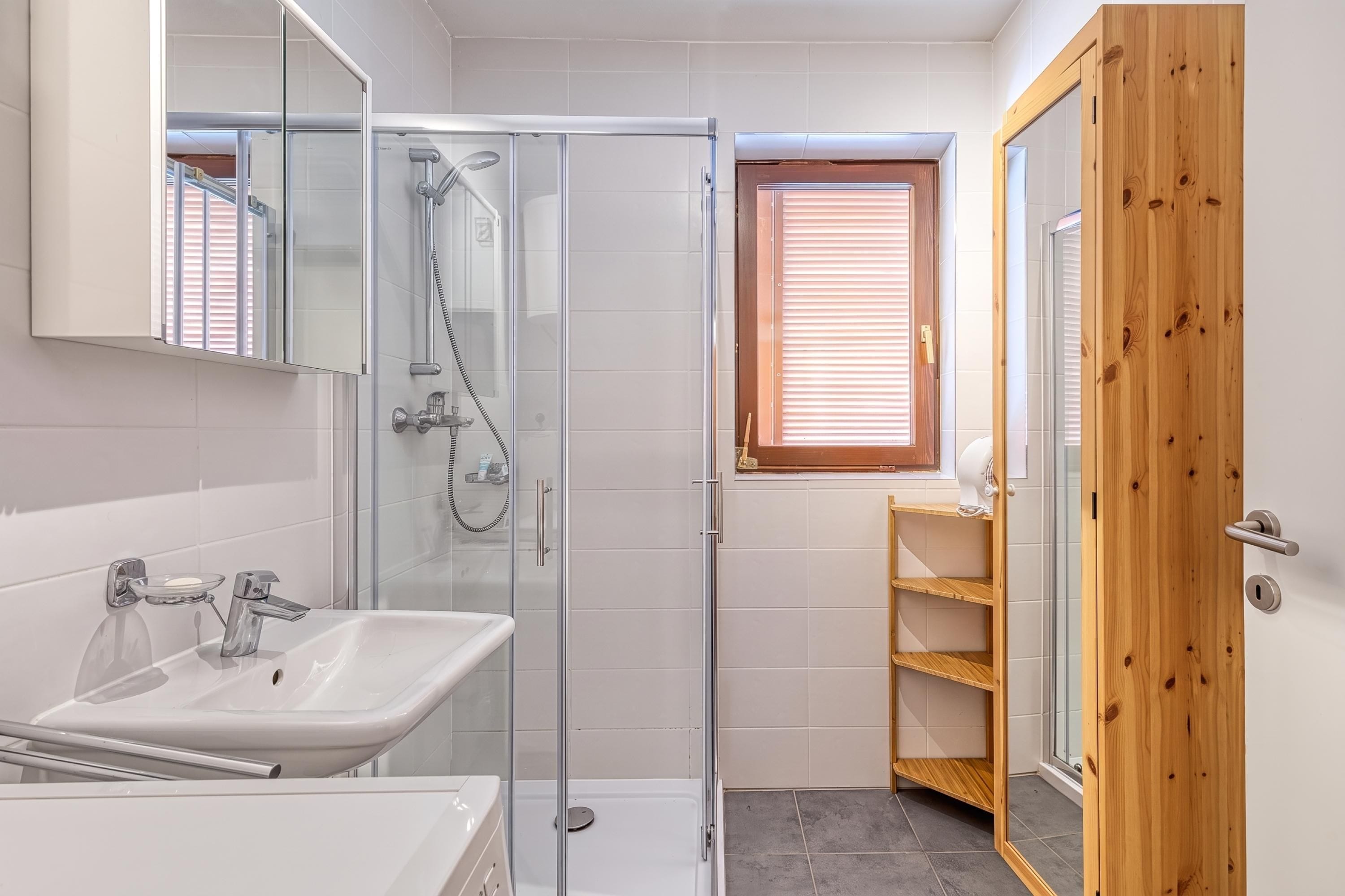 A modern bathroom with a glass-enclosed shower, a white sink, and a wooden door.