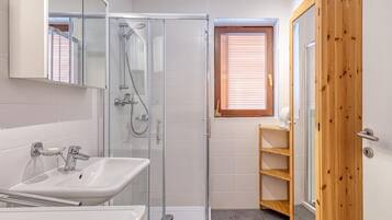 A modern bathroom with a glass-enclosed shower, a white sink, and a wooden door.