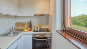 A kitchen with white cabinets, a stove, an oven, and a window with a view of greenery.