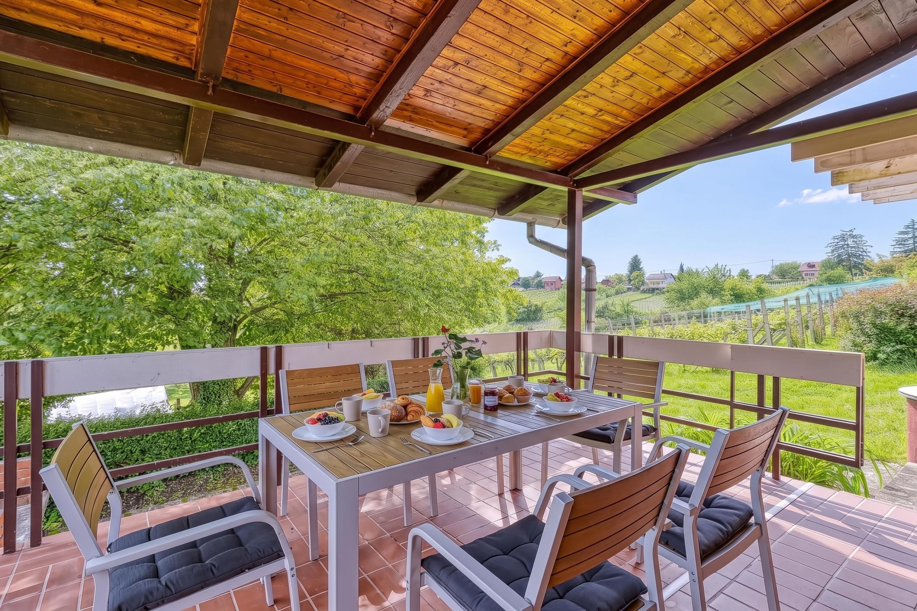 A covered outdoor dining area with a table set for breakfast, surrounded by chairs.