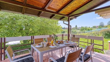 A covered outdoor dining area with a table set for breakfast, surrounded by chairs.