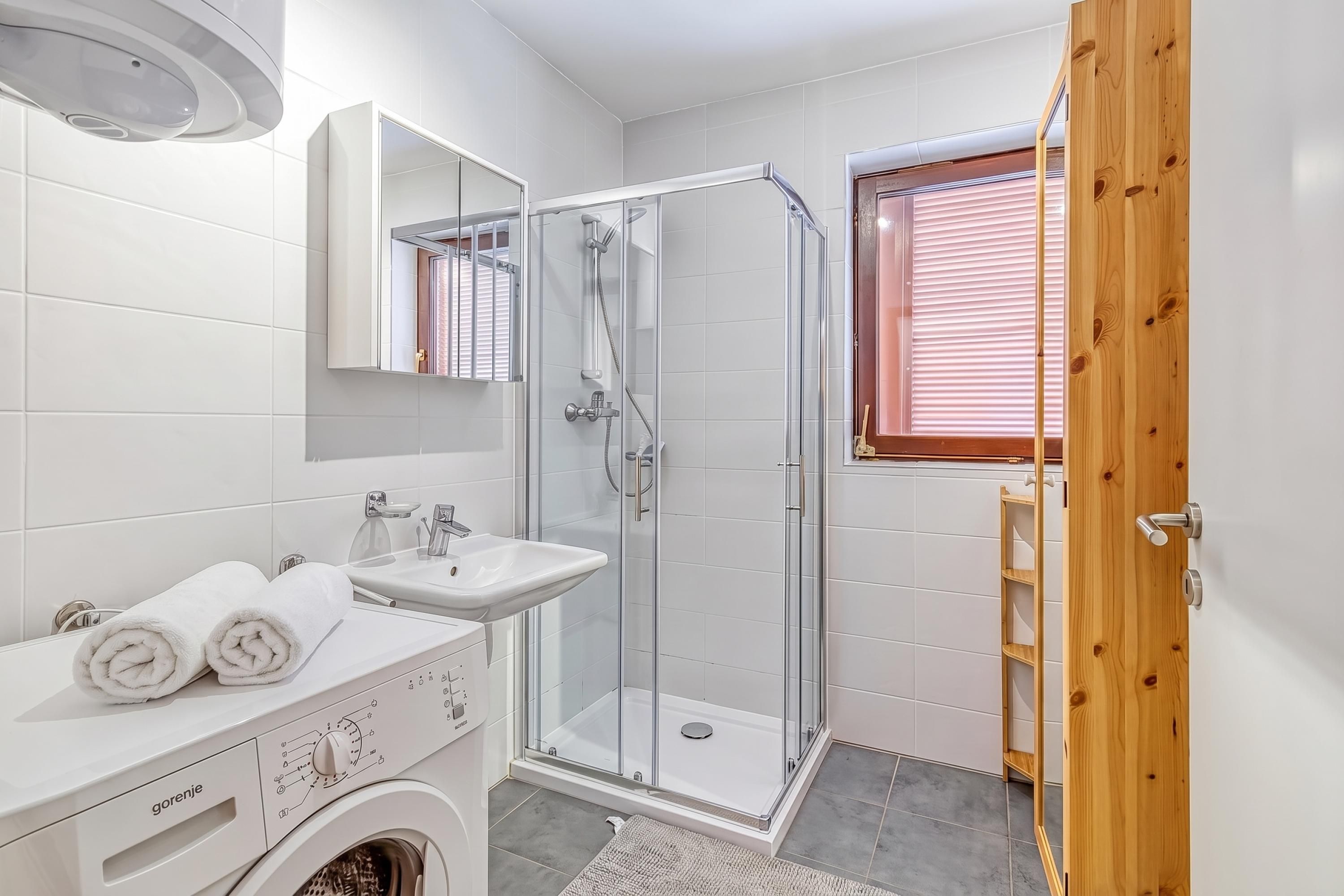 Ein modernes Badezimmer mit Duschkabine aus Glas, einem Waschbecken und einer Waschmaschine.