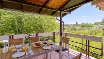 Deck de madeira com mesa posta para café da manhã, com vista para um jardim exuberante e edifícios ao longe.