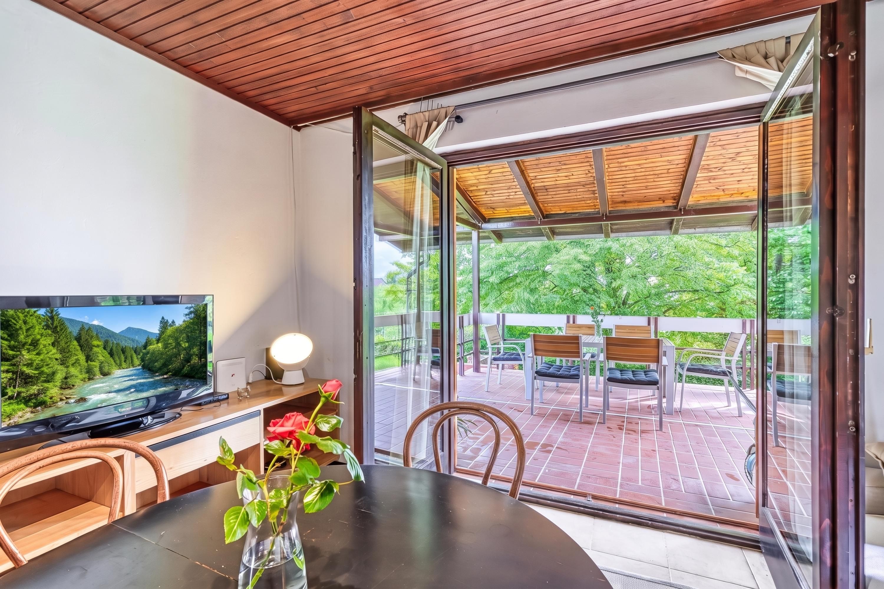 A modern room with a television, a desk, a chair, and a glass door leading to an outdoor patio with a table and chairs.