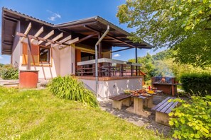Una casa moderna con un patio cubierto, una parrilla al aire libre y un jardín.