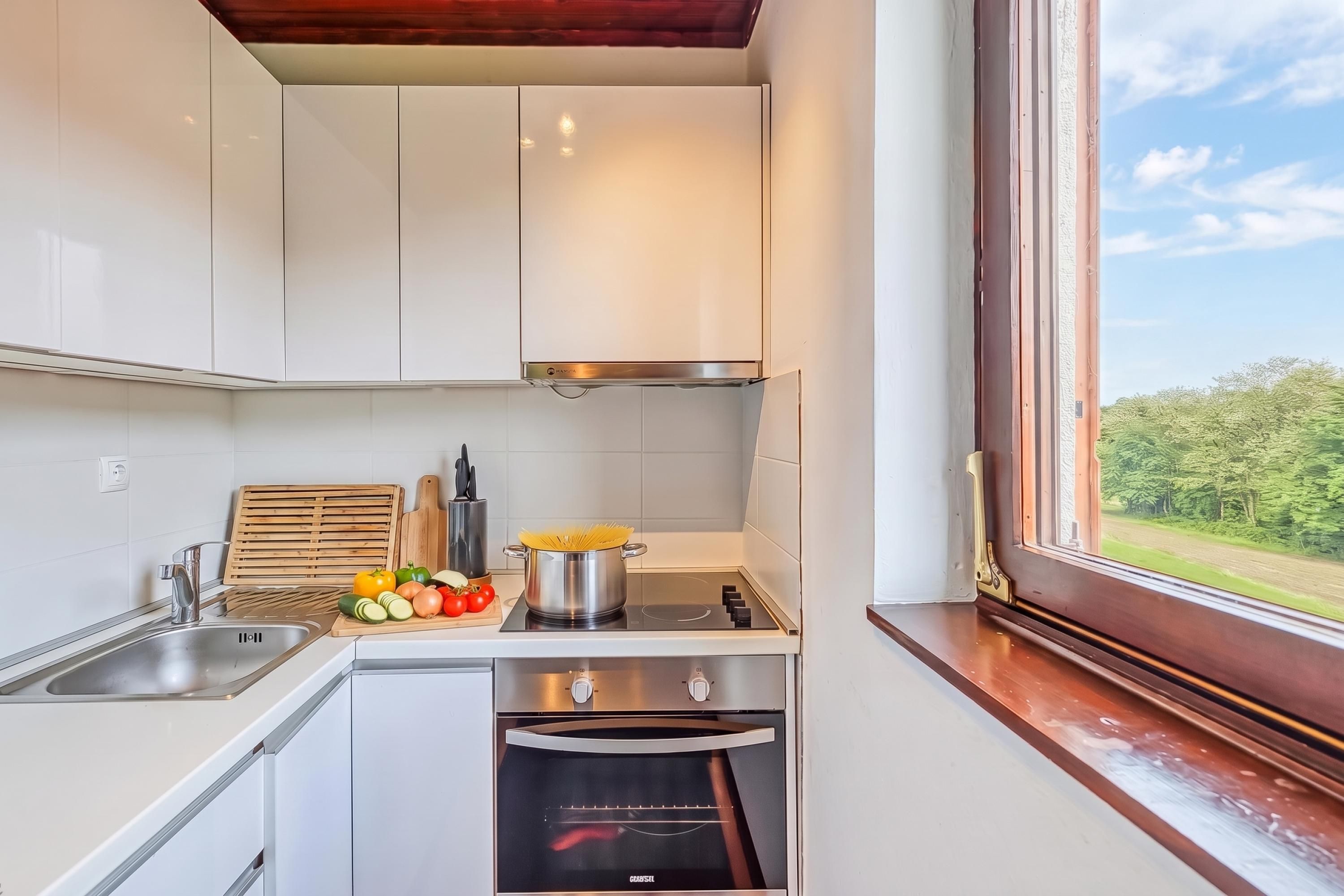 Cocina moderna con gabinetes blancos, estufa de acero inoxidable y vista al exterior a través de una ventana.