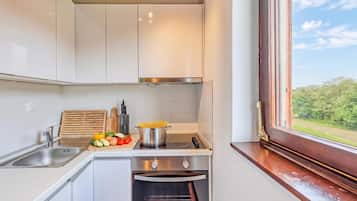Cocina moderna con gabinetes blancos, estufa de acero inoxidable y vista al exterior a través de una ventana.