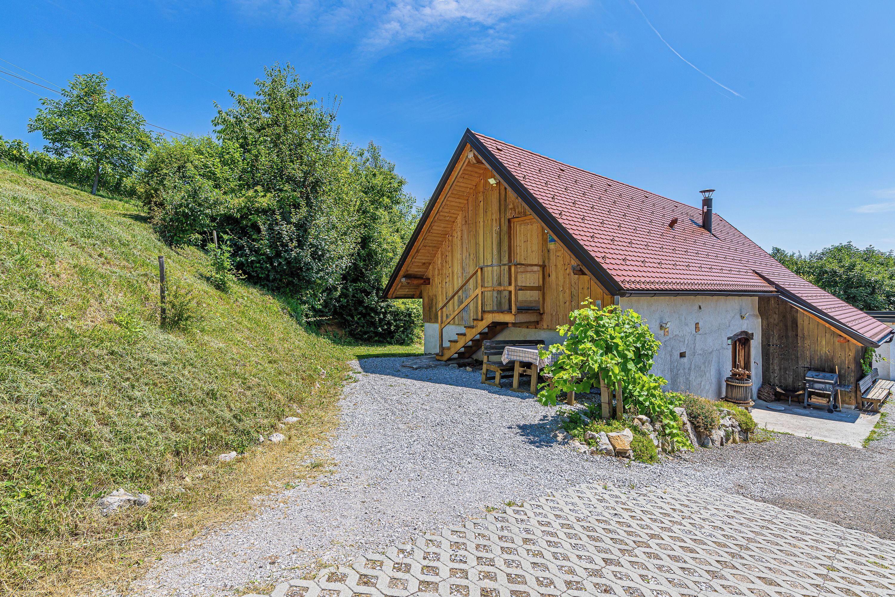 A wooden cabin with a red roof, a gravel driveway, and a wooden staircase leading to the entrance.