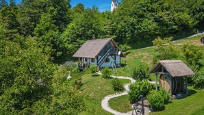 Ländliche Szenerie mit zwei traditionellen Holzhäusern, einer Kirche im Hintergrund und einem gewundenen Pfad.