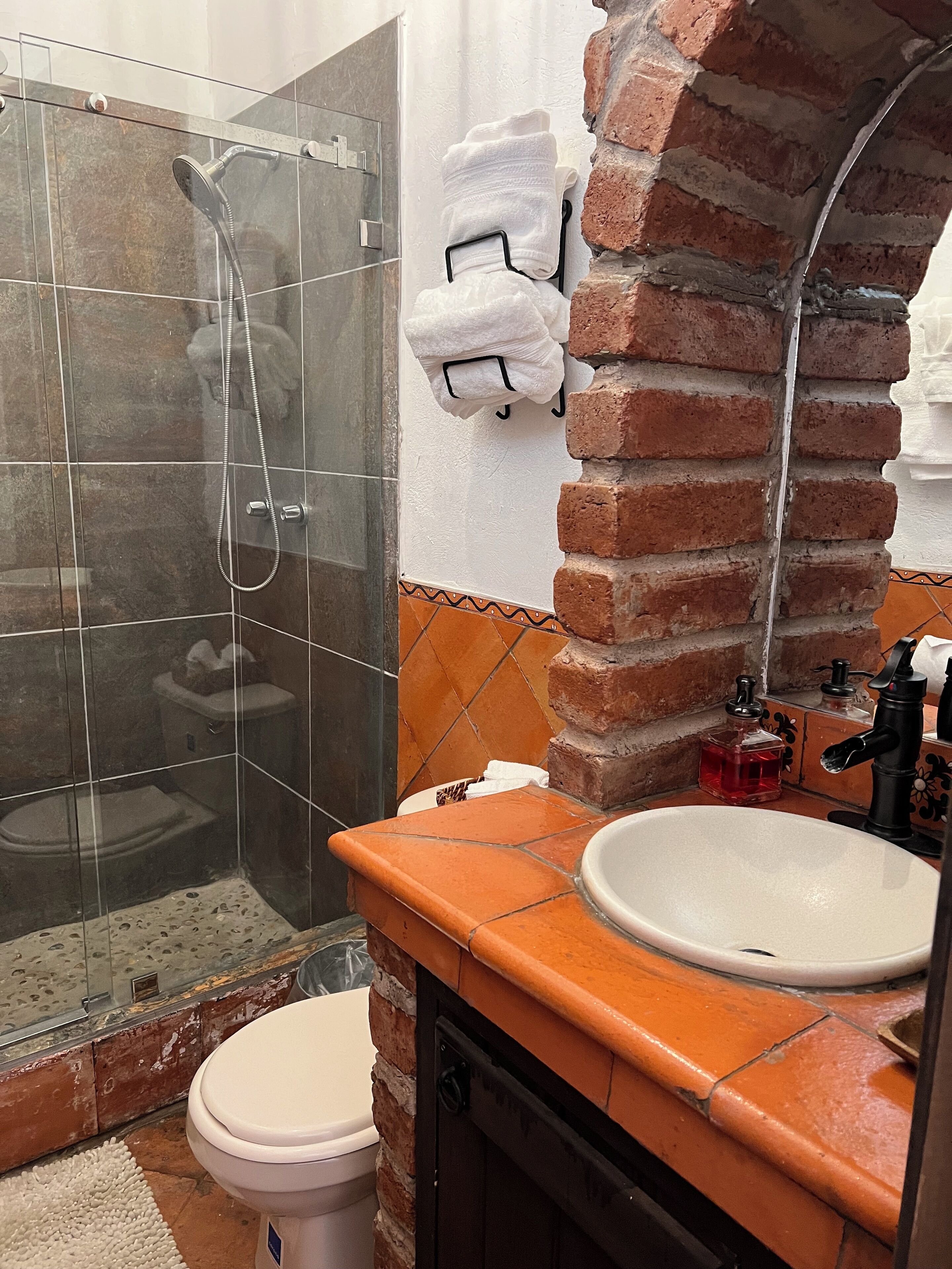 Un baño con ducha envuelta en vidrio, inodoro blanco y lavamanos con grifo negro.