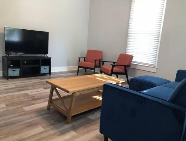 A living room with a wooden coffee table, blue armchairs, a black entertainment unit with a TV, and red chairs. - Whole home, sleeps 7, pets ok, Wi-Fi, Full Kitchen (Sac City)