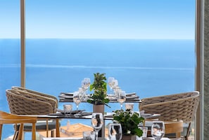 A dining table set with chairs, a potted plant, and a view of the sea. - Ajul Luxury Hotel & Spa Resort Registry Collection (Kassandra)