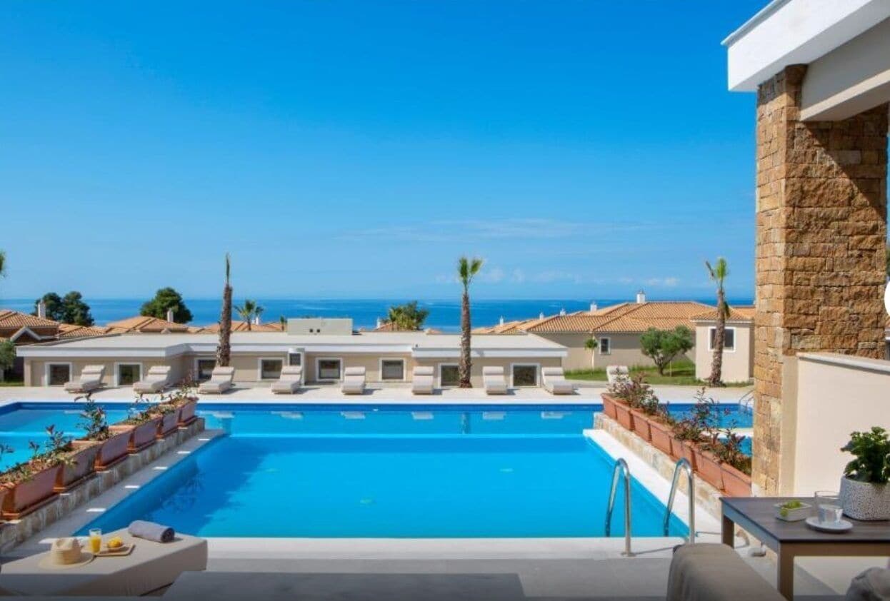A swimming pool with lounge chairs, a view of the sea, and a stone wall.