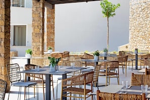 An outdoor dining area with wicker chairs and tables, stone pillars, and potted plants. - Ajul Luxury Hotel & Spa Resort Registry Collection (Kassandra)