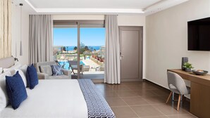 Habitación de hotel con cama, escritorio, silla, televisor y vista a una piscina y paisaje.