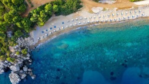 An aerial view of a beach with rows of umbrellas and a rocky shoreline. - Ajul Luxury Hotel & Spa Resort Registry Collection (Kassandra)