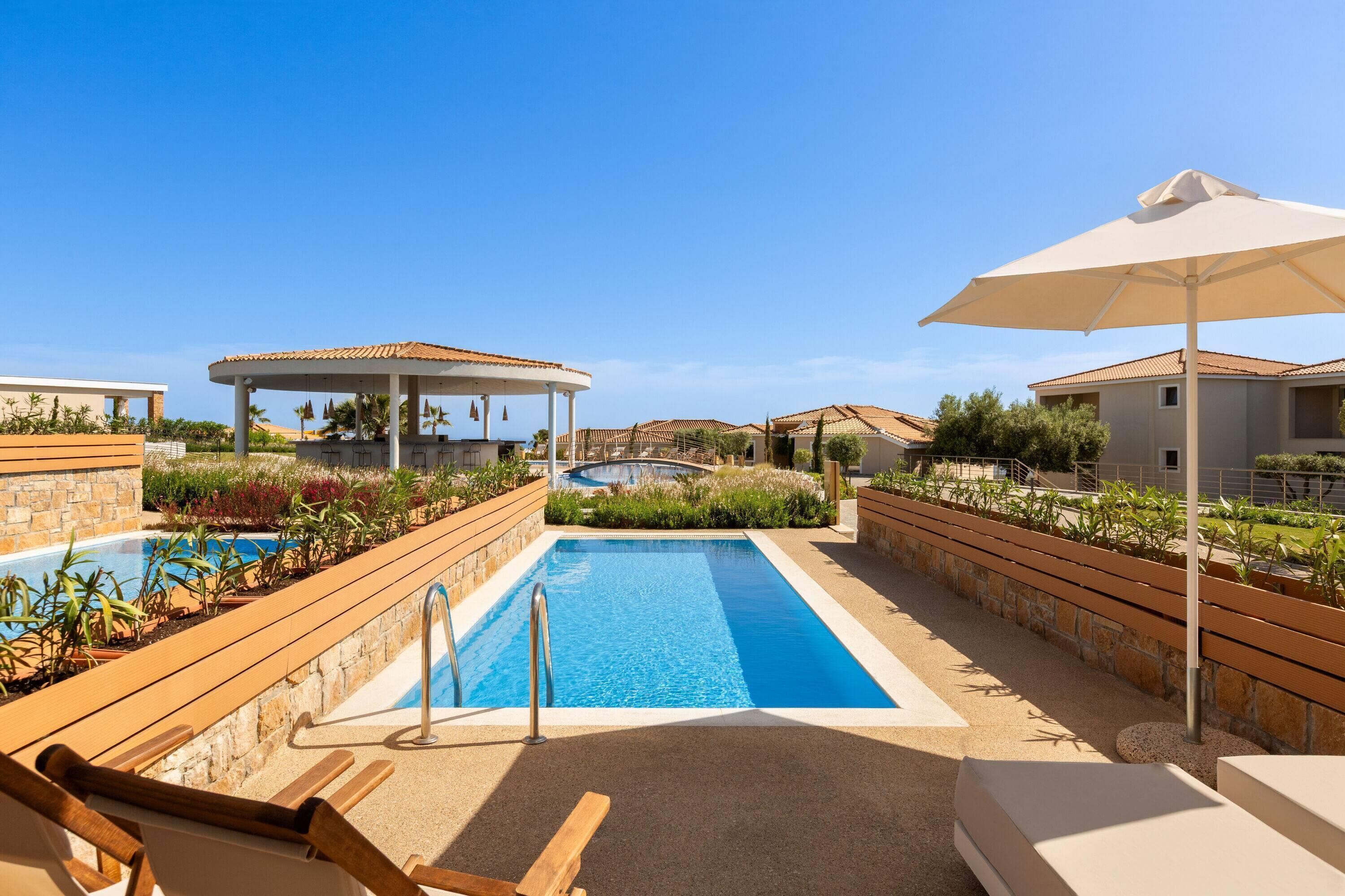 A swimming pool with a sun lounger and umbrella, surrounded by plants and a gazebo.