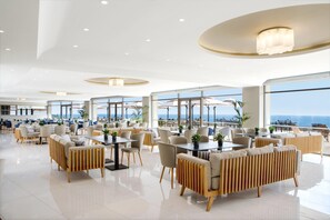 A spacious, well-lit restaurant with modern furniture and large windows offering ocean views. - Ajul Luxury Hotel & Spa Resort Registry Collection (Kassandra)