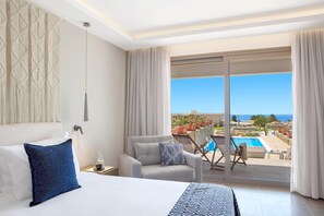 A hotel room with a bed, a sofa, a view of the pool and ocean, and a balcony with potted plants. - Ajul Luxury Hotel & Spa Resort Registry Collection (Kassandra)