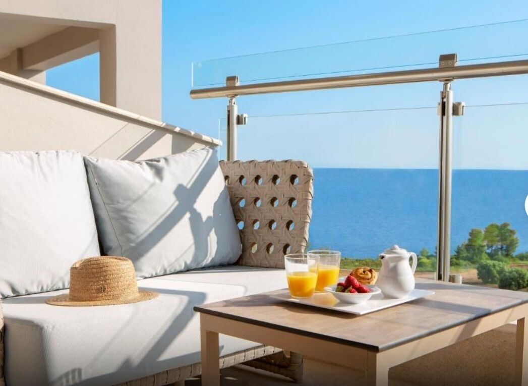 A balcony with a sofa, a table with breakfast, and a view of the sea.