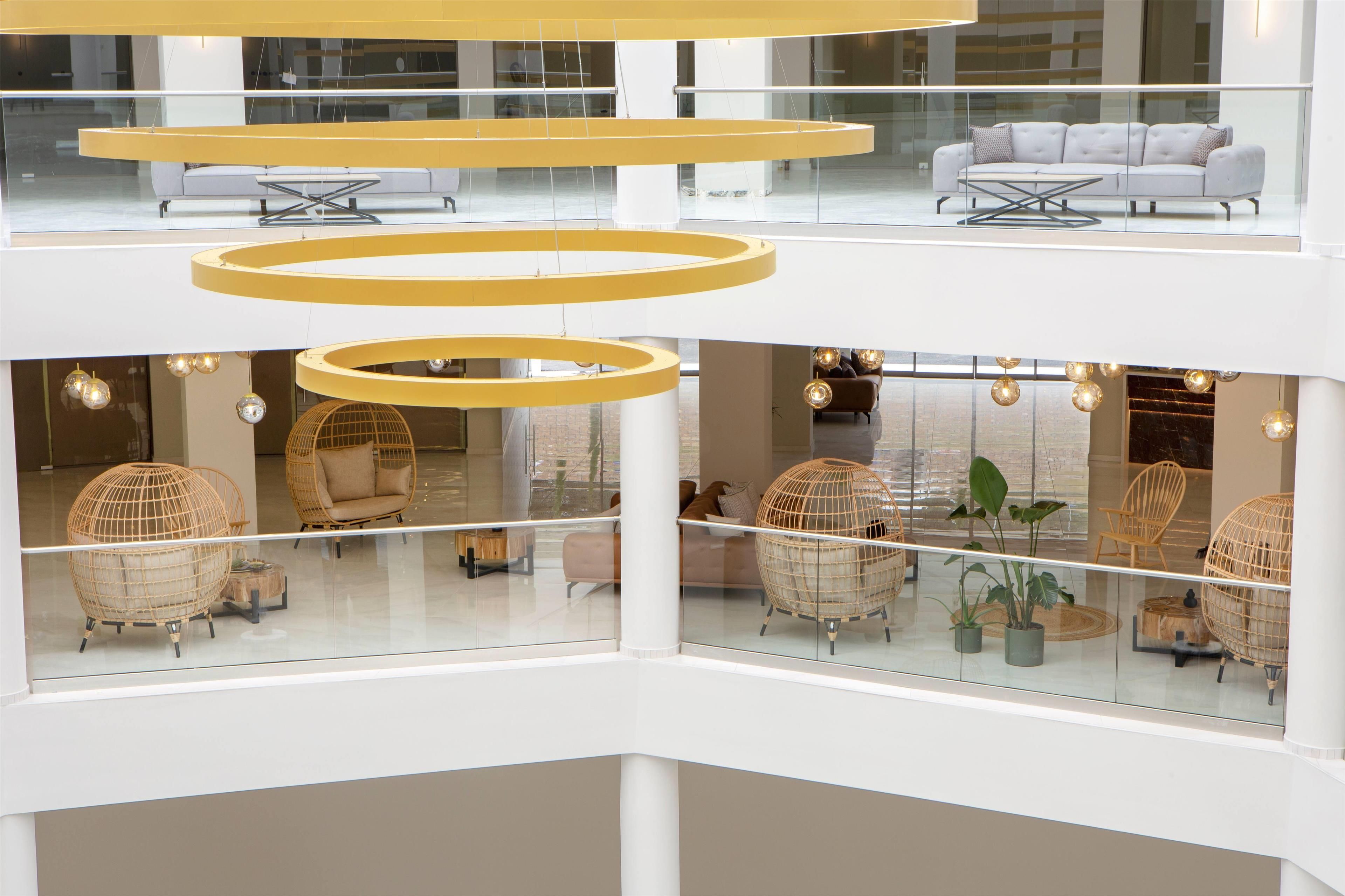 A multi-level interior with glass railings, circular yellow light fixtures, wicker furniture, and a white sofa.