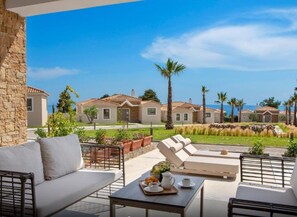 A patio area with outdoor furniture, a stone wall, and a view of a residential complex with multiple houses and palm trees. - Ajul Luxury Hotel & Spa Resort Registry Collection (Kassandra)