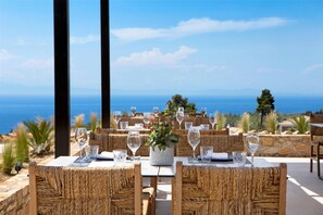 An outdoor dining area with wicker furniture, a table with a vase of flowers, and a view of the sea.