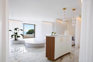 A modern interior with a curved seating area, a central island with a plant, and a view through a large window.
