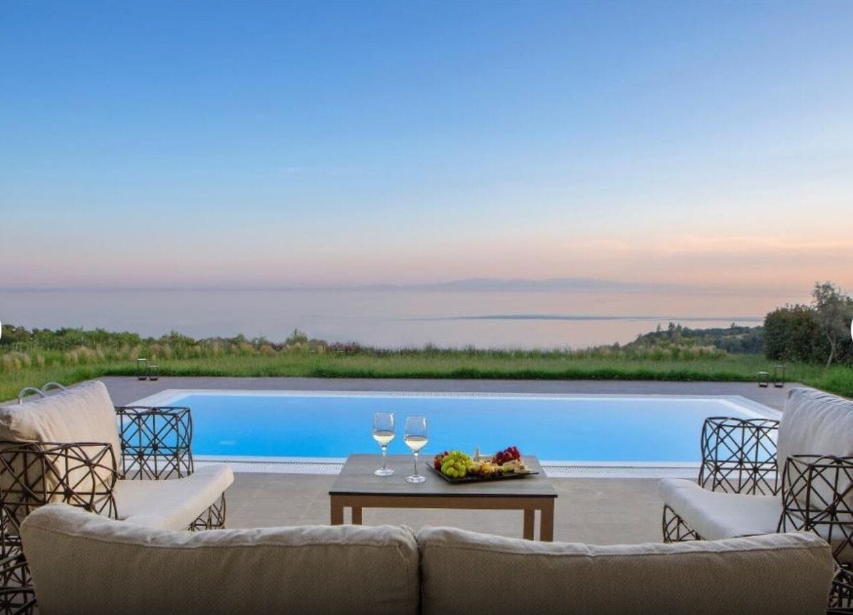 A poolside seating area with a table, two glasses, and a fruit platter.