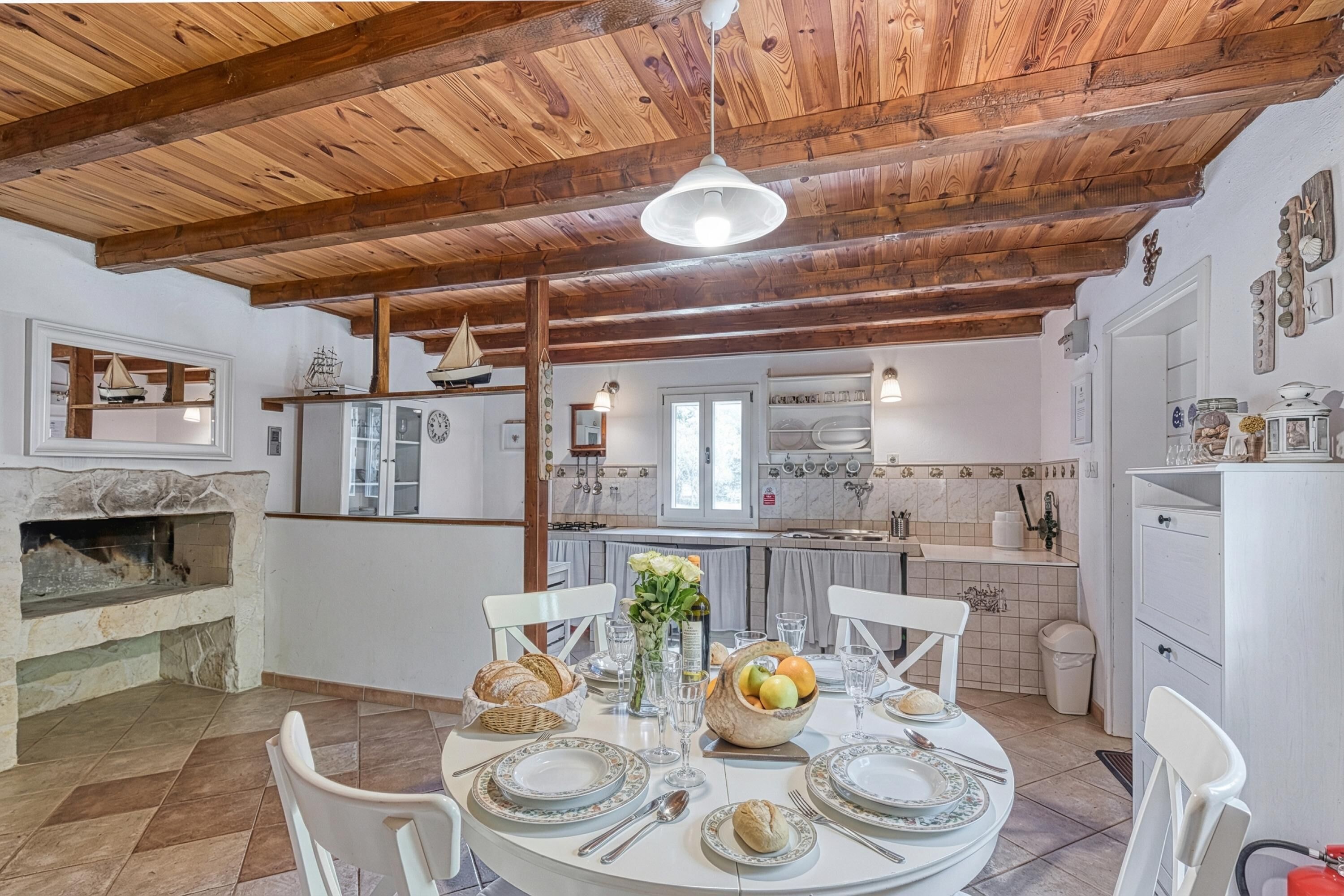 A dining area with a wooden ceiling, a fireplace, and a kitchen in the background.