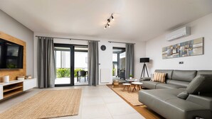 A modern living room with a grey sofa, a flat-screen TV, a coffee table, and a dining area with a table and chairs. - Villa Bella with heated pool and Seaview (Klimno (Krk))