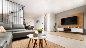 A modern living room with a grey sofa, a round coffee table with a plant, a TV on a wooden wall, and a staircase with glass railings. - Villa Bella with heated pool and Seaview (Klimno (Krk))