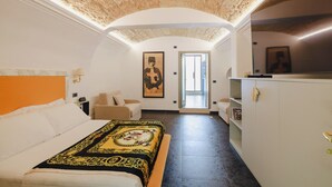 A hotel room with a bed, a sofa, a painting, a television, and a view of the outside. - Incentro Domus (Polignano a Mare)