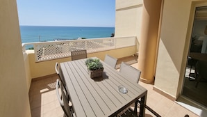 Un balcon avec une table et des chaises, une plante en pot et une vue sur la mer.