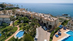Un hôtel situé sur la côte, composé de plusieurs bâtiments, doté d’une piscine et offrant une vue sur la mer.