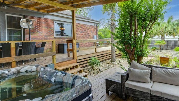 Un patio cubierto con jacuzzi, mobiliario exterior y vistas a una casa de ladrillo.