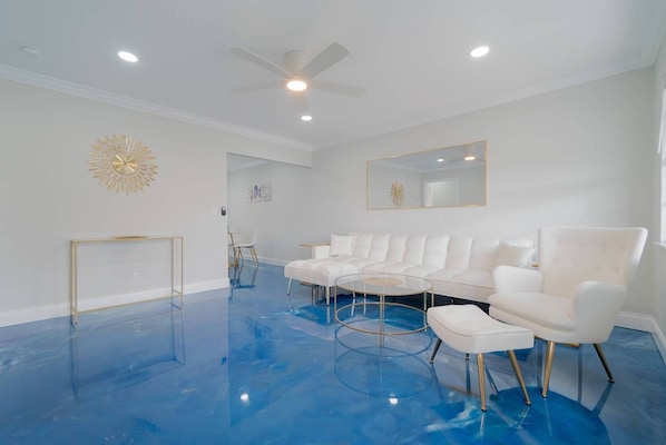 A modern living room with a white sofa set, a glass coffee table, and a ceiling fan.