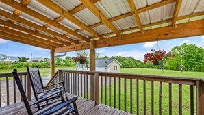 A wooden deck with a pergola overhead, overlooking a grassy yard with a house and a hanging flower basket. - Perfect Guntersville Retreat Near Tennessee River! (Guntersville)