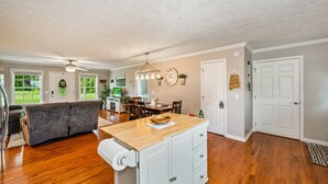 A spacious living area with a wooden floor, a sofa, a dining table, and a kitchen island with cabinets. - Perfect Guntersville Retreat Near Tennessee River! (Guntersville)