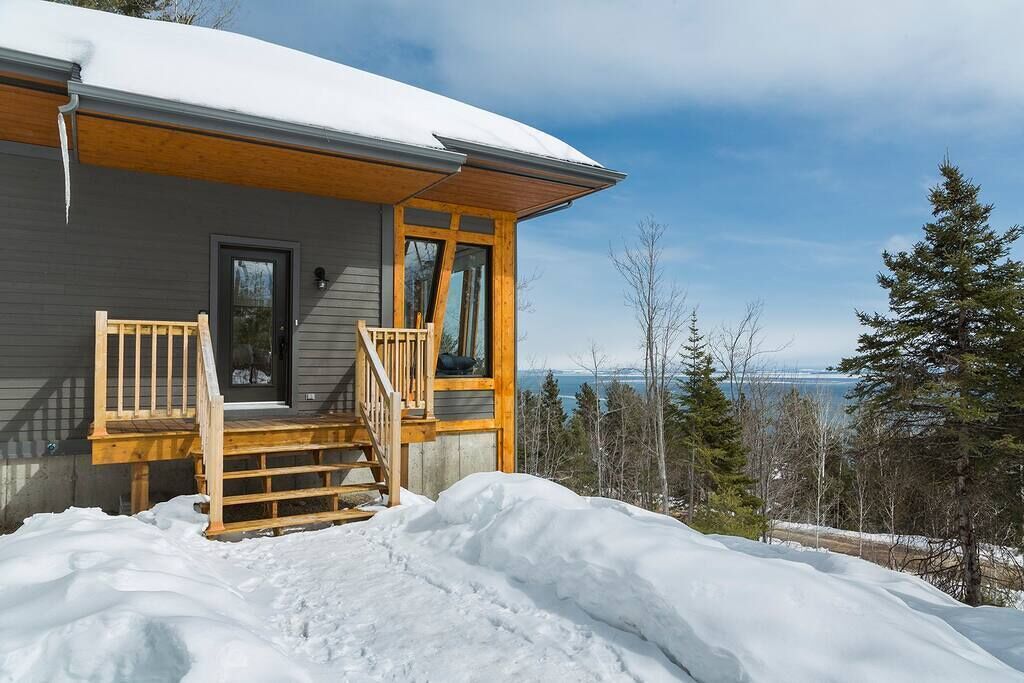 A cabin with a wooden porch, a door, and a view of a lake and trees.