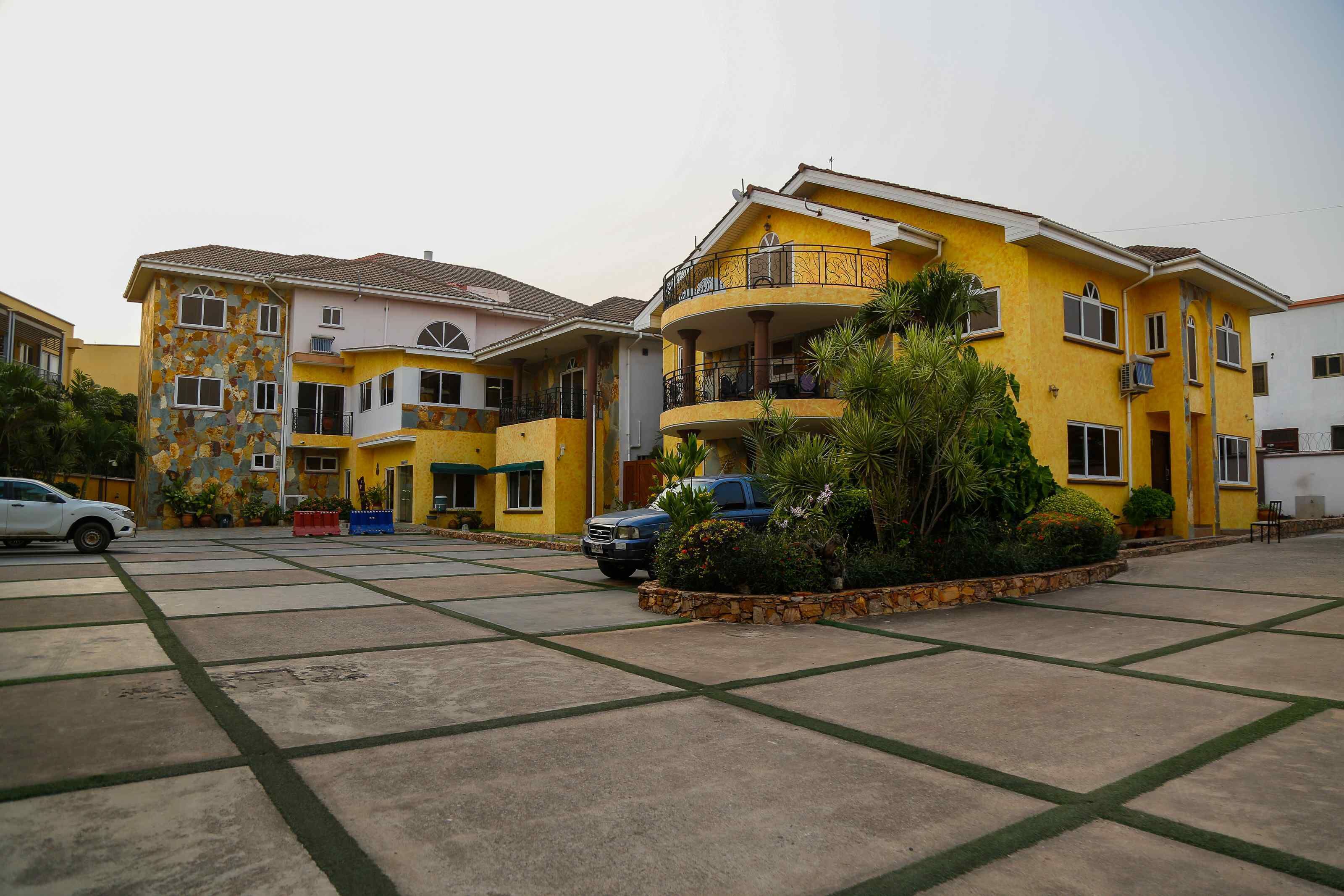A residential building with multiple balconies, a parking area, and a well-maintained garden.
