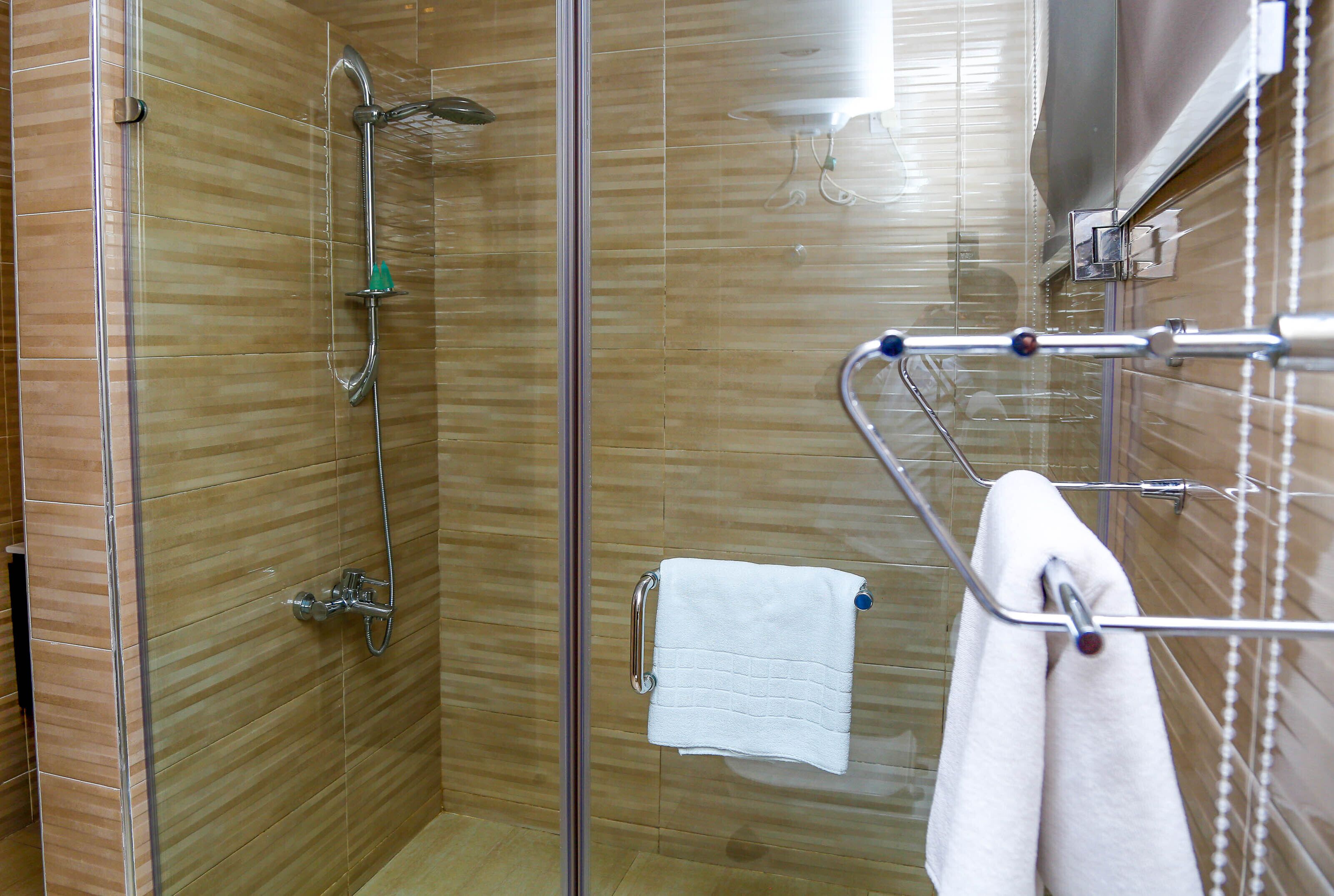 A glass-enclosed shower with a handheld showerhead and a wall-mounted faucet.