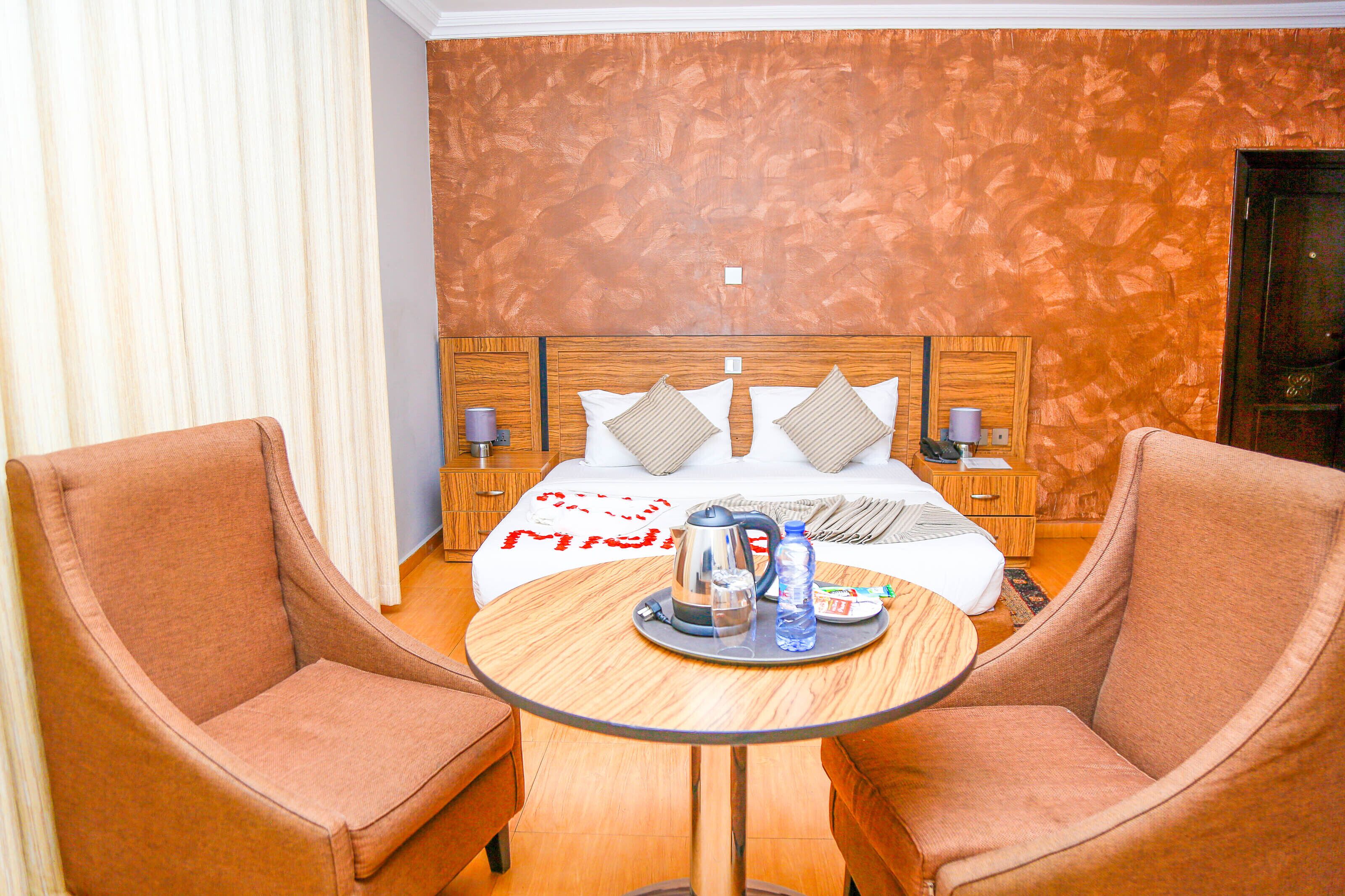 Een hotelkamer met een bed, twee fauteuils, een ronde tafel met een dienblad ontbijtartikelen en een houten hoofdbord.