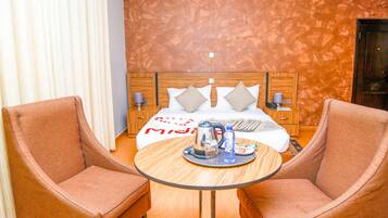 Een hotelkamer met een bed, twee fauteuils, een ronde tafel met een dienblad ontbijtartikelen en een houten hoofdbord.