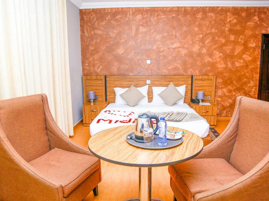 Een hotelkamer met een bed, twee fauteuils, een ronde tafel met een dienblad ontbijtartikelen en een houten hoofdbord.
